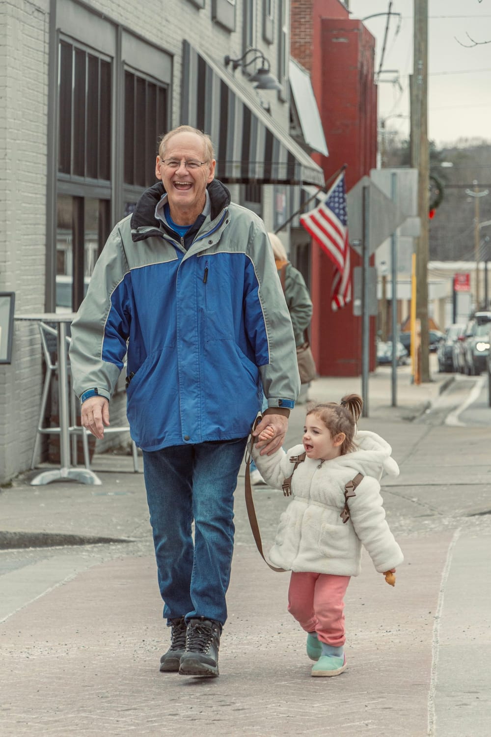 An older man walking outdoors hand in hand with a young girl